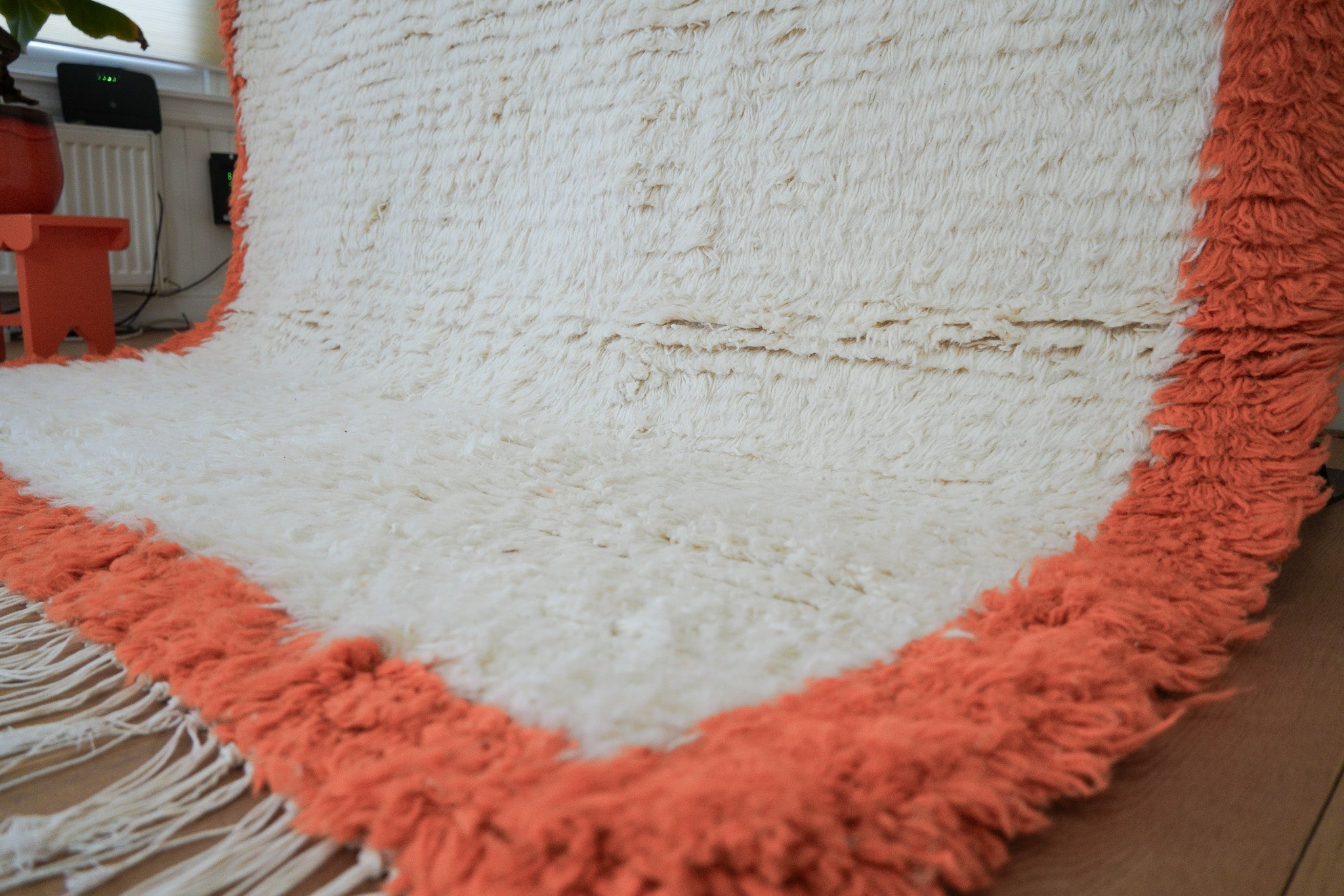 Corner view of the Aisha rug showing shaggy orange fringe, handwoven wool texture, and knotted cream wool pattern on wooden floor