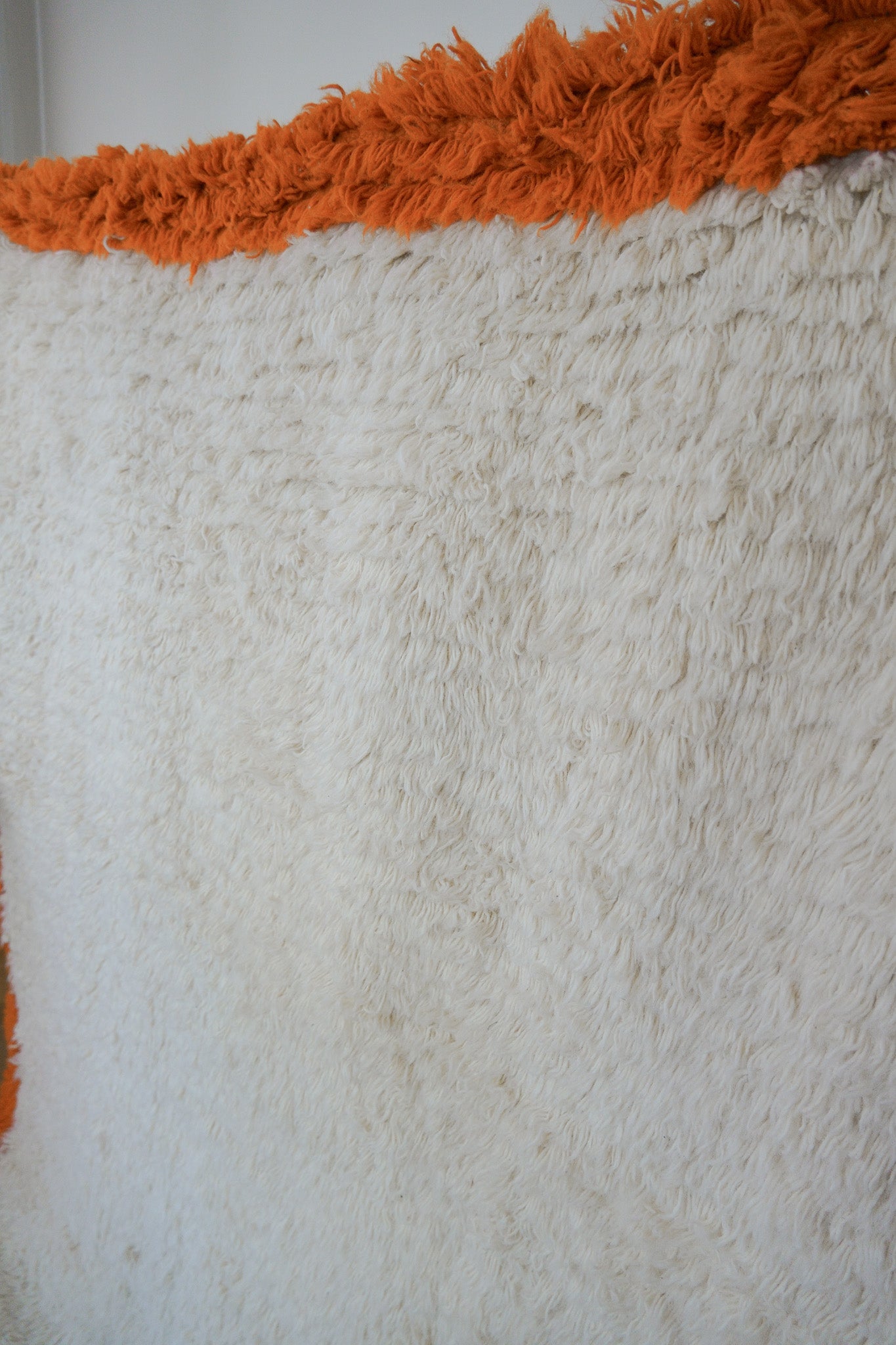 Close-up of the Aisha rug texture showing thick high-pile cream wool and orange border detail