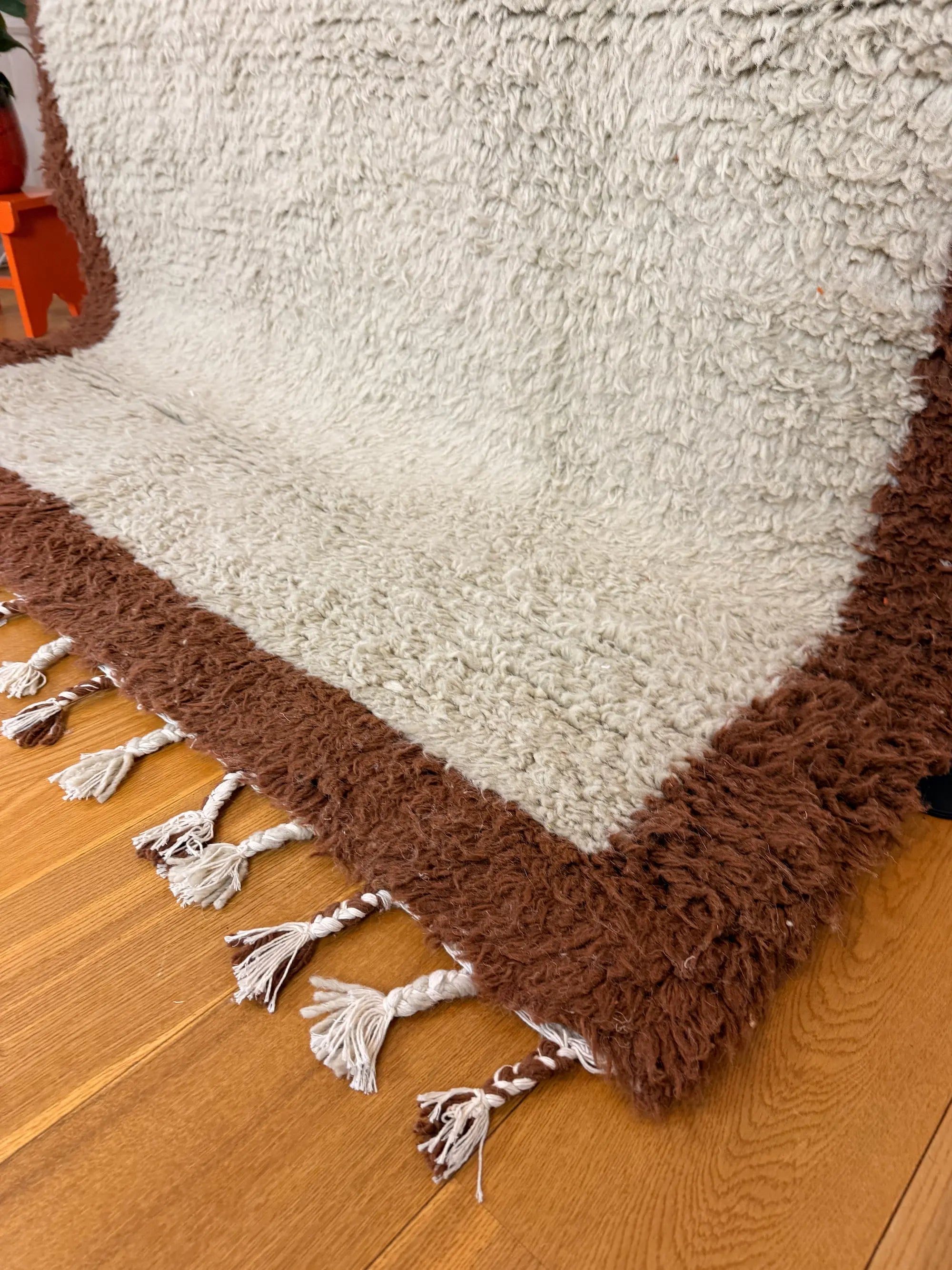 Close-up of Aliyah handmade Berber wool rug showing the cream wool pile, chocolate brown border and hand-knotted fringe, Tunisia.
