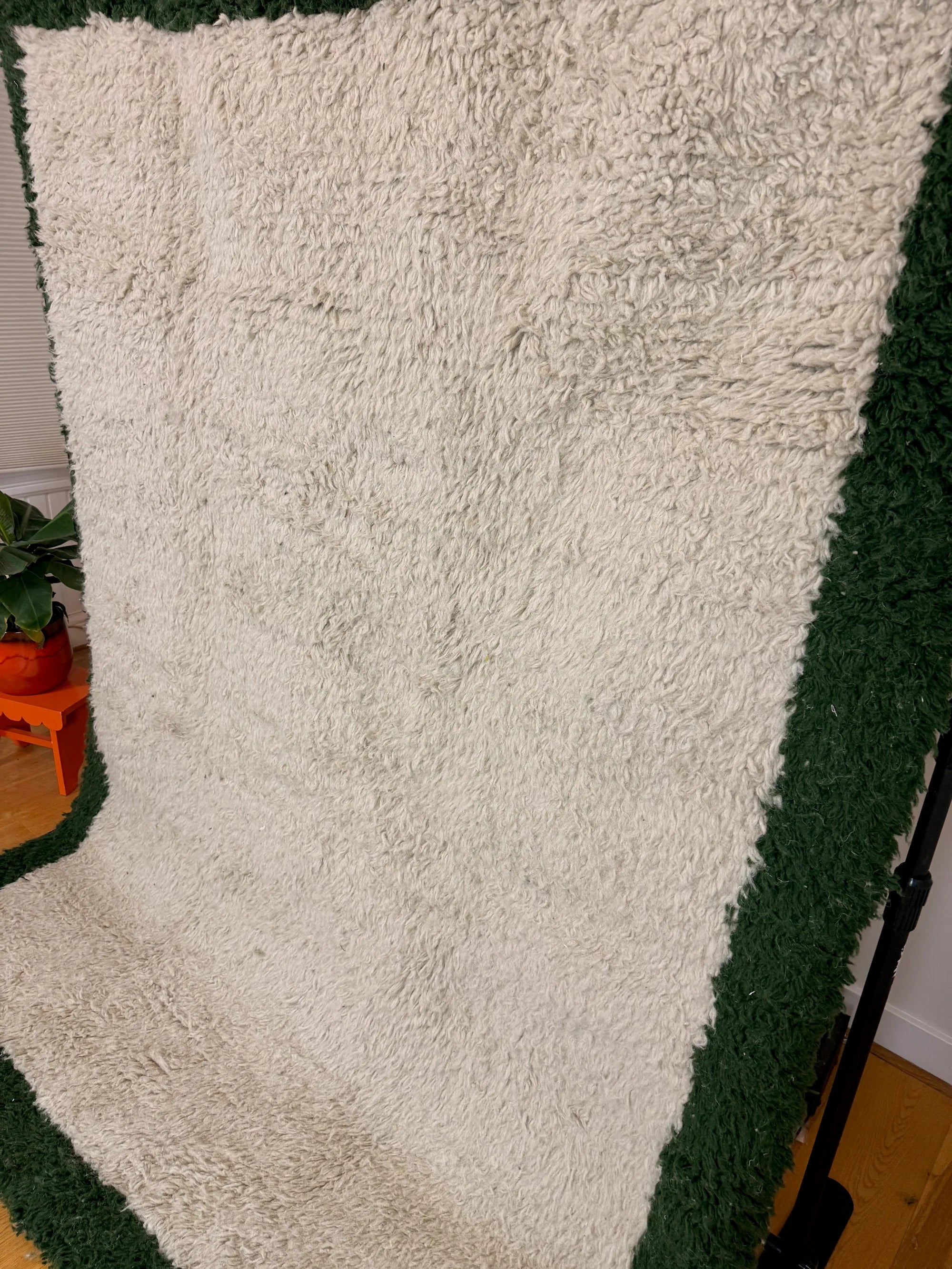 Bochra handmade shaggy Berber wool rug, side view showing the full cream centre framed by a deep forest green border, handmade in Tunisia.