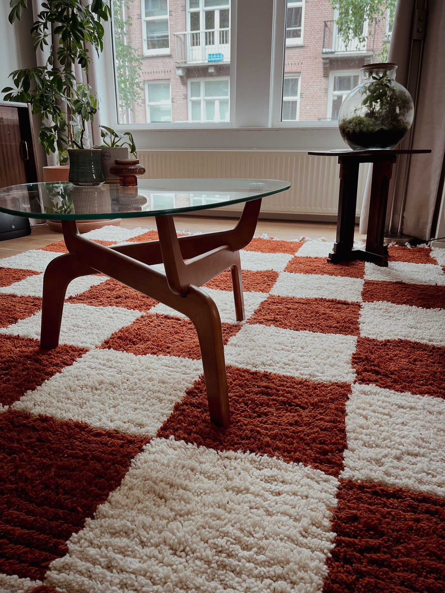 Burnt red orange and cream checkered rug under round wooden coffee table in a light-filled room