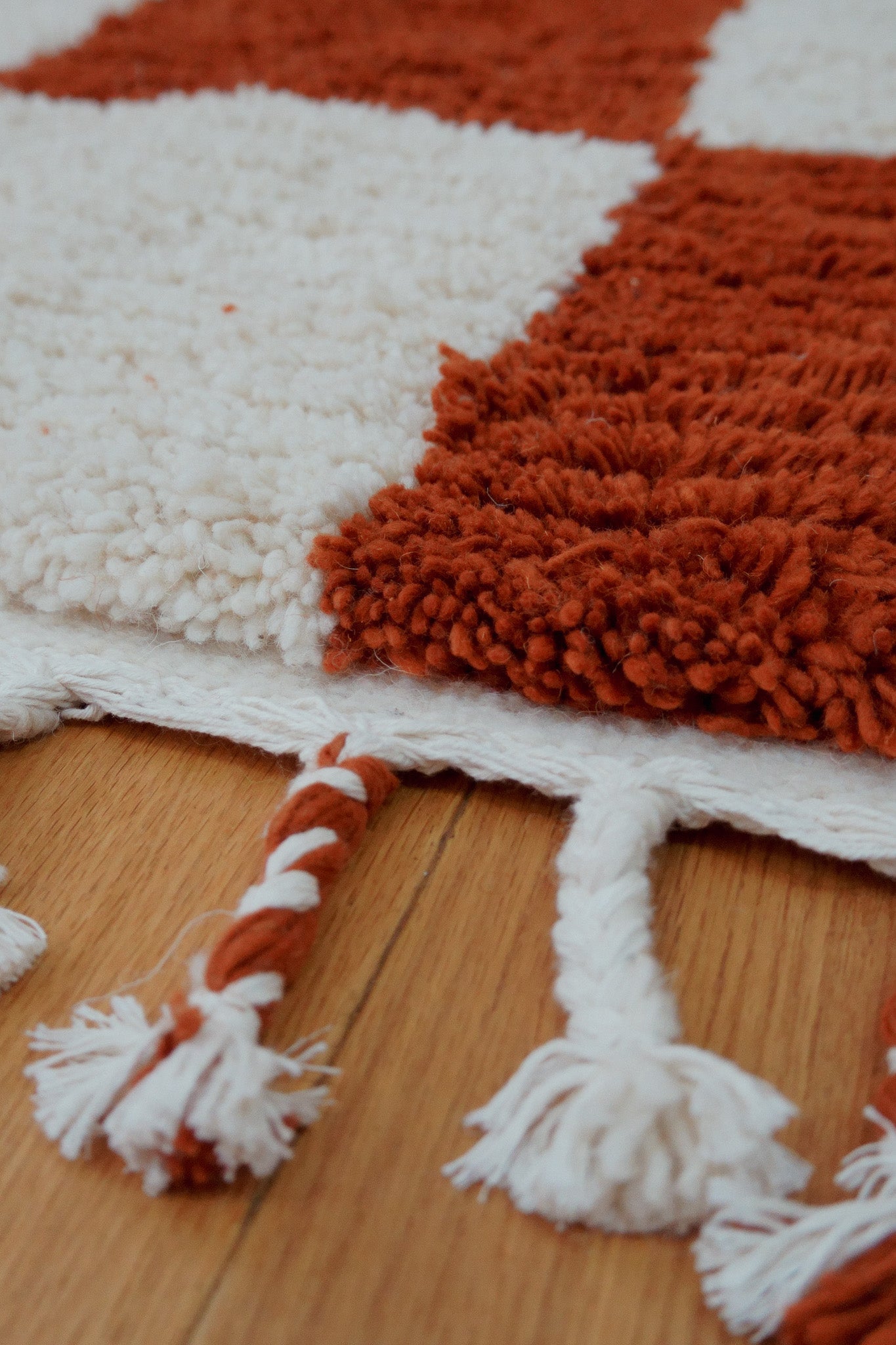 Close-up of the rug's corner with knotted fringe and thick wool pile in burnt orange and cream
