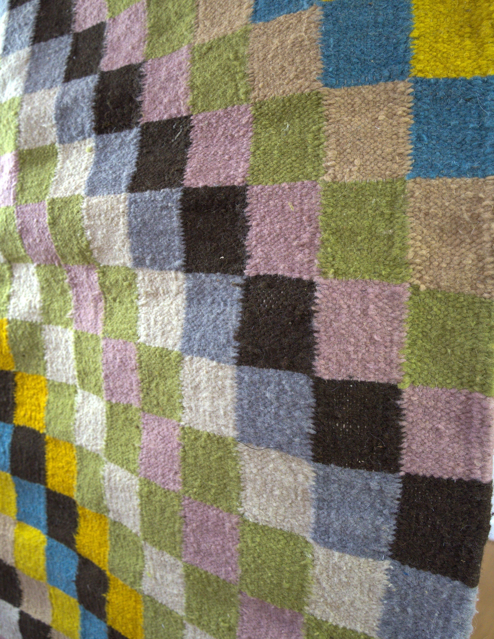 Close-up of the Hiba rug corner showing intricate checkered weave and plush wool texture in colorful tones