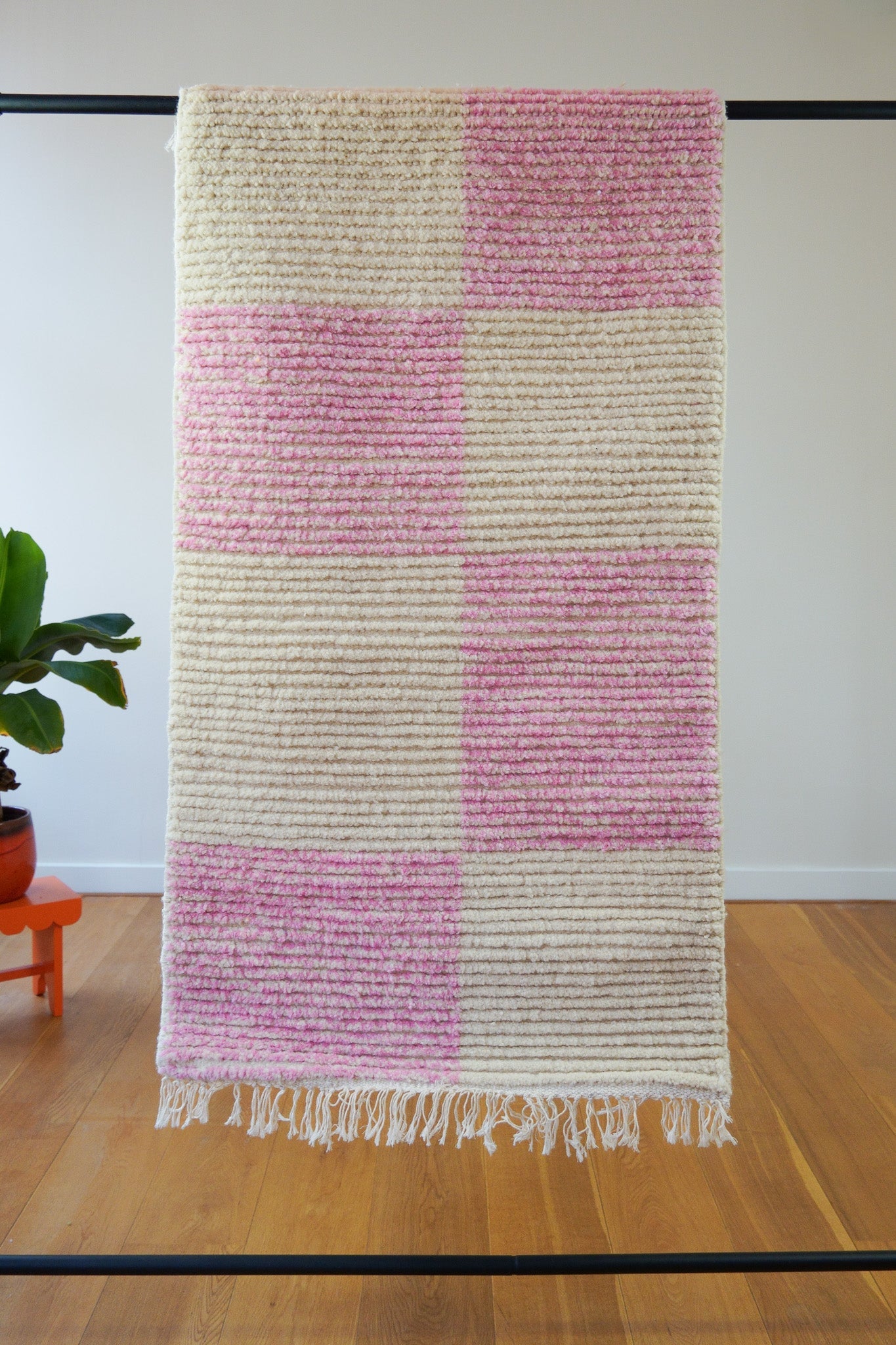 Full front view of Lina handmade checkered wool rug in pink and off-white, hanging flat with fringes visible on a wooden floor