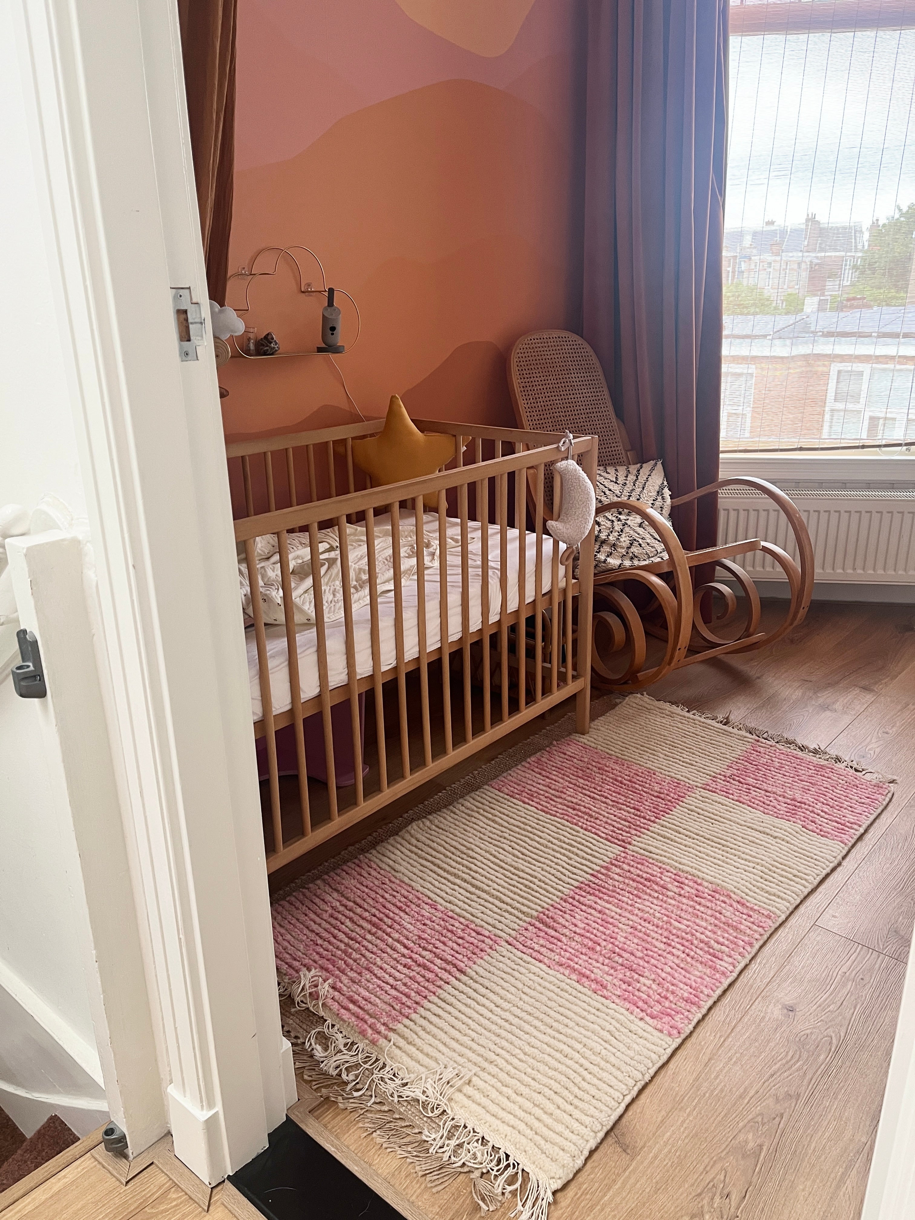 Lina handmade pink and off-white wool rug styled in a nursery room beside a wooden crib, adding warmth and softness