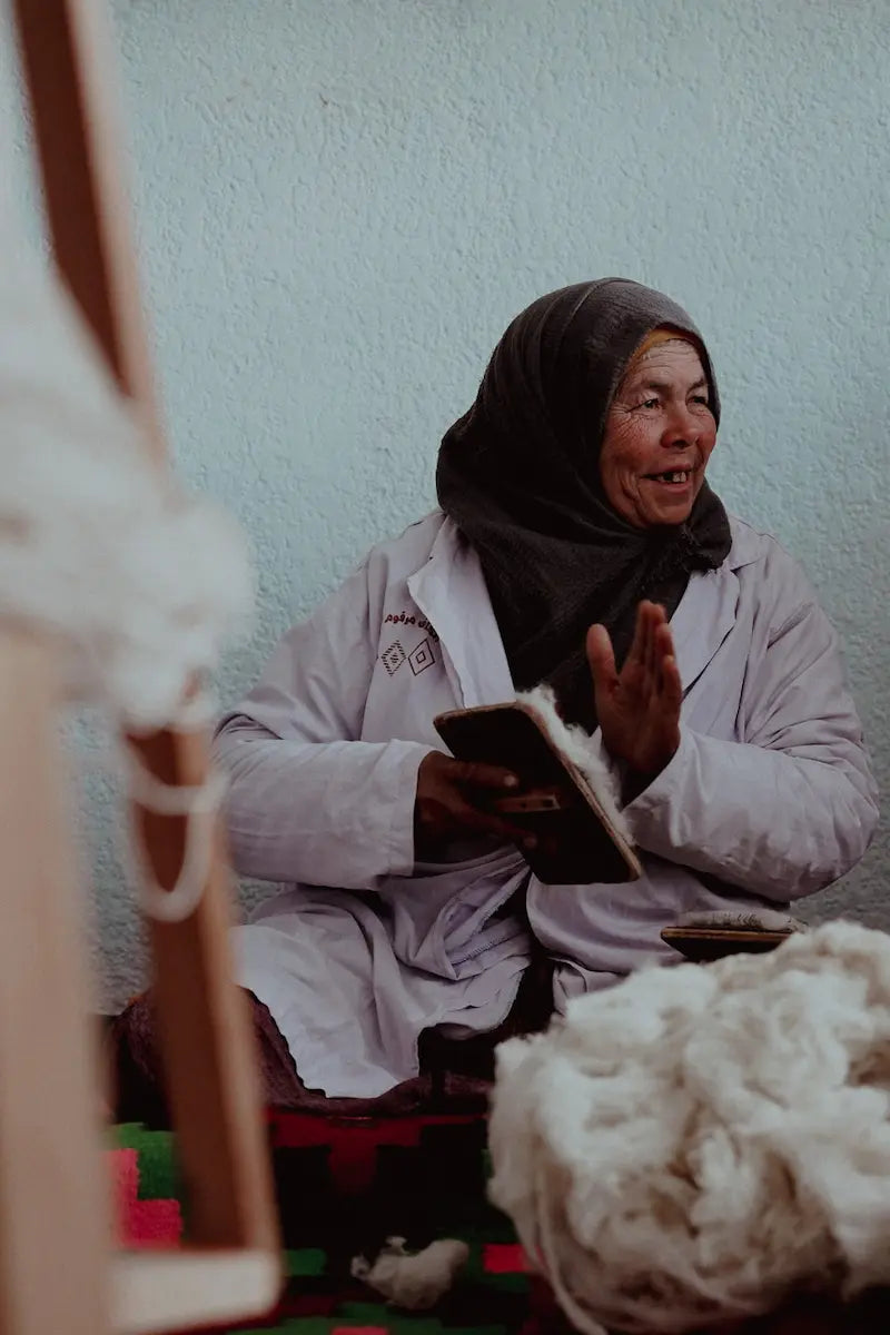 Woman sitting and using a tool to work the wool with a white wall background