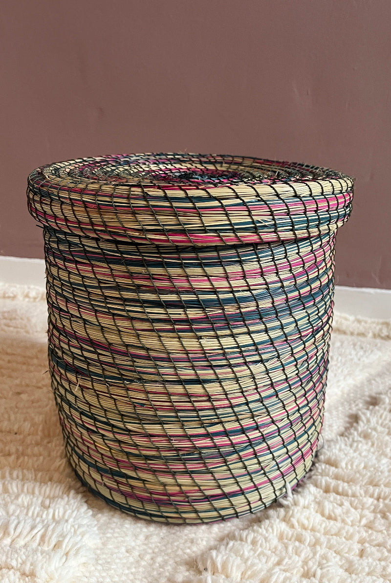 Handmade straw basket Yara in pink, green, and cream, full view. With matching lid, made from natural straw and wire, displayed on a soft textile surface.