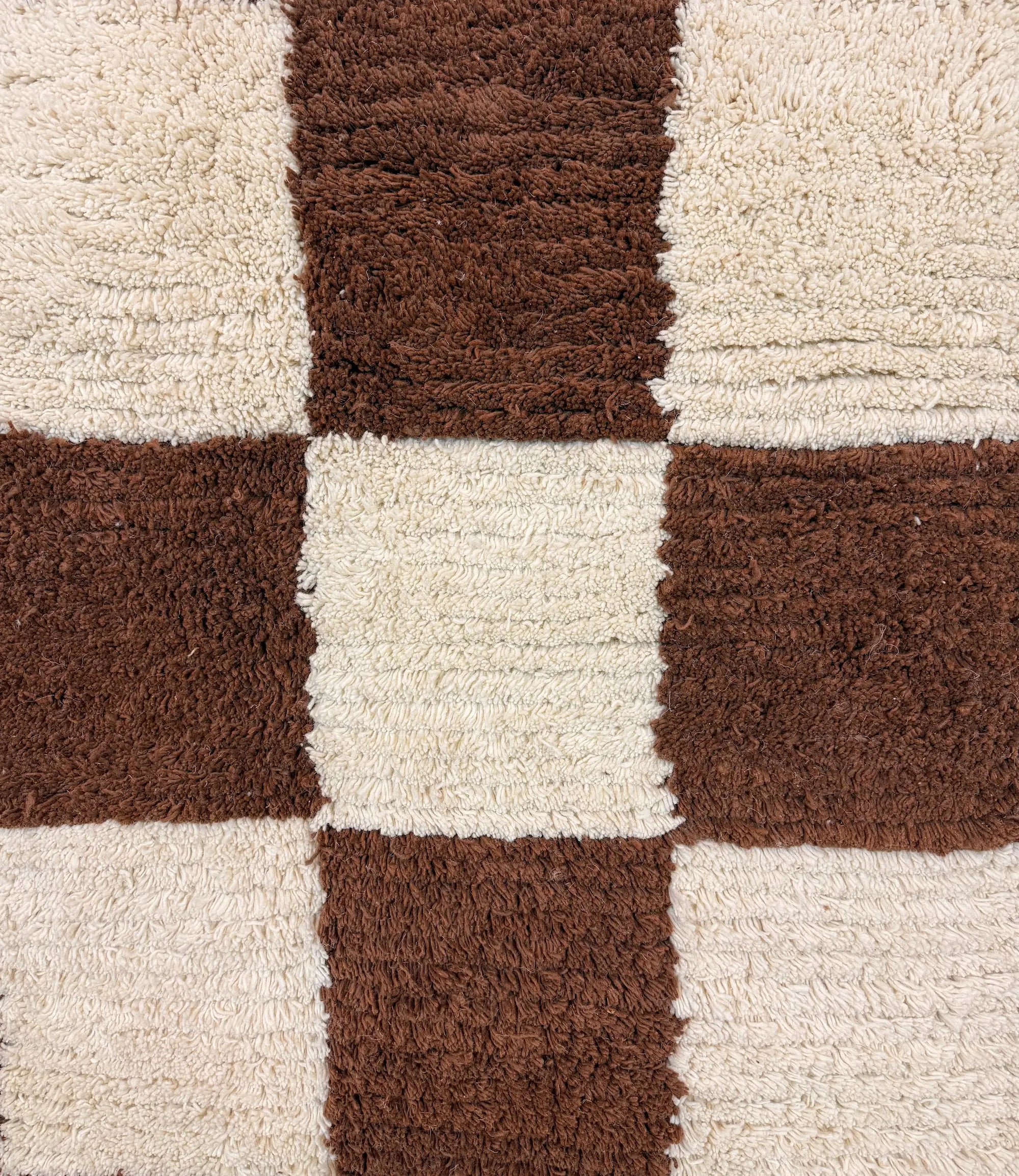 Macro close-up of the checkerboard squares on the Meriem Berber wool rug, revealing the hand-knotted wool texture in chocolate brown and natural white.
