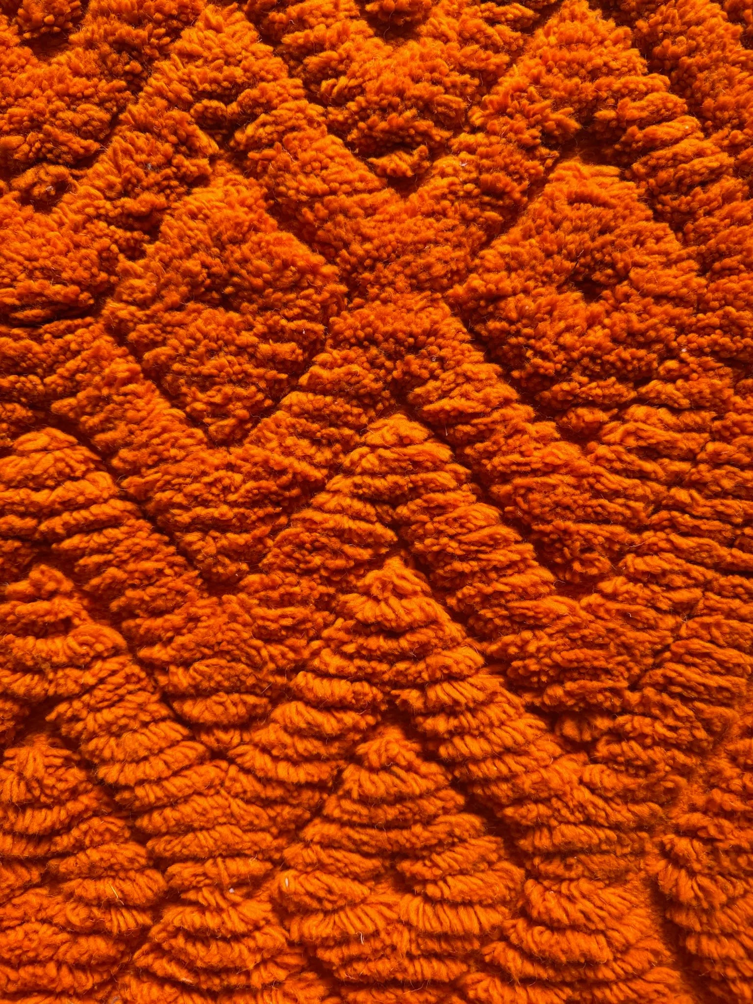 Macro close-up of the raised Amazigh diamond pattern on the Mira handmade Berber wool rug, burnt orange wool texture, Tunisia.