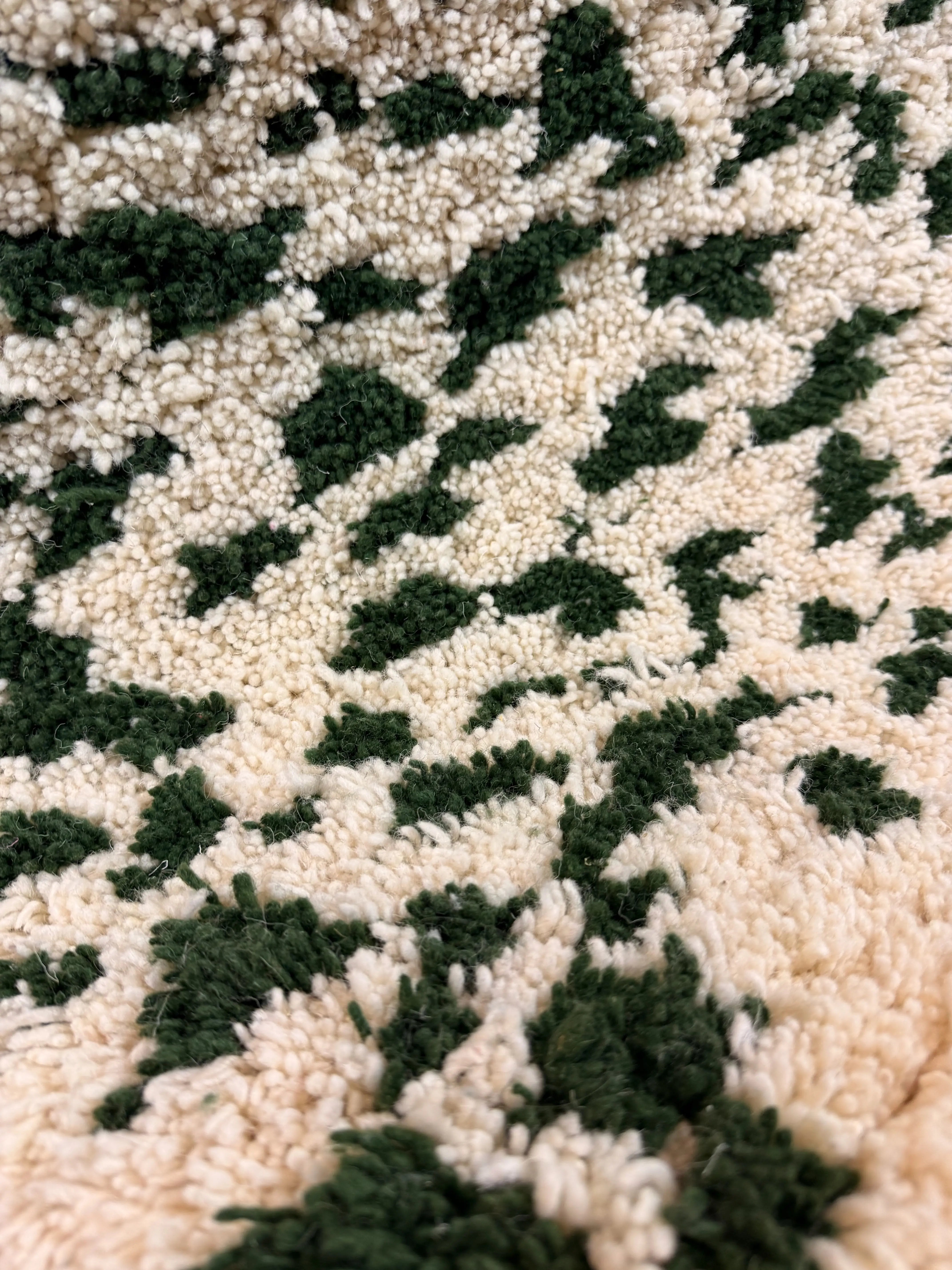 Macro close-up of the scattered green and cream spot pattern on the Mouna handmade shaggy Berber wool rug, Tunisia.