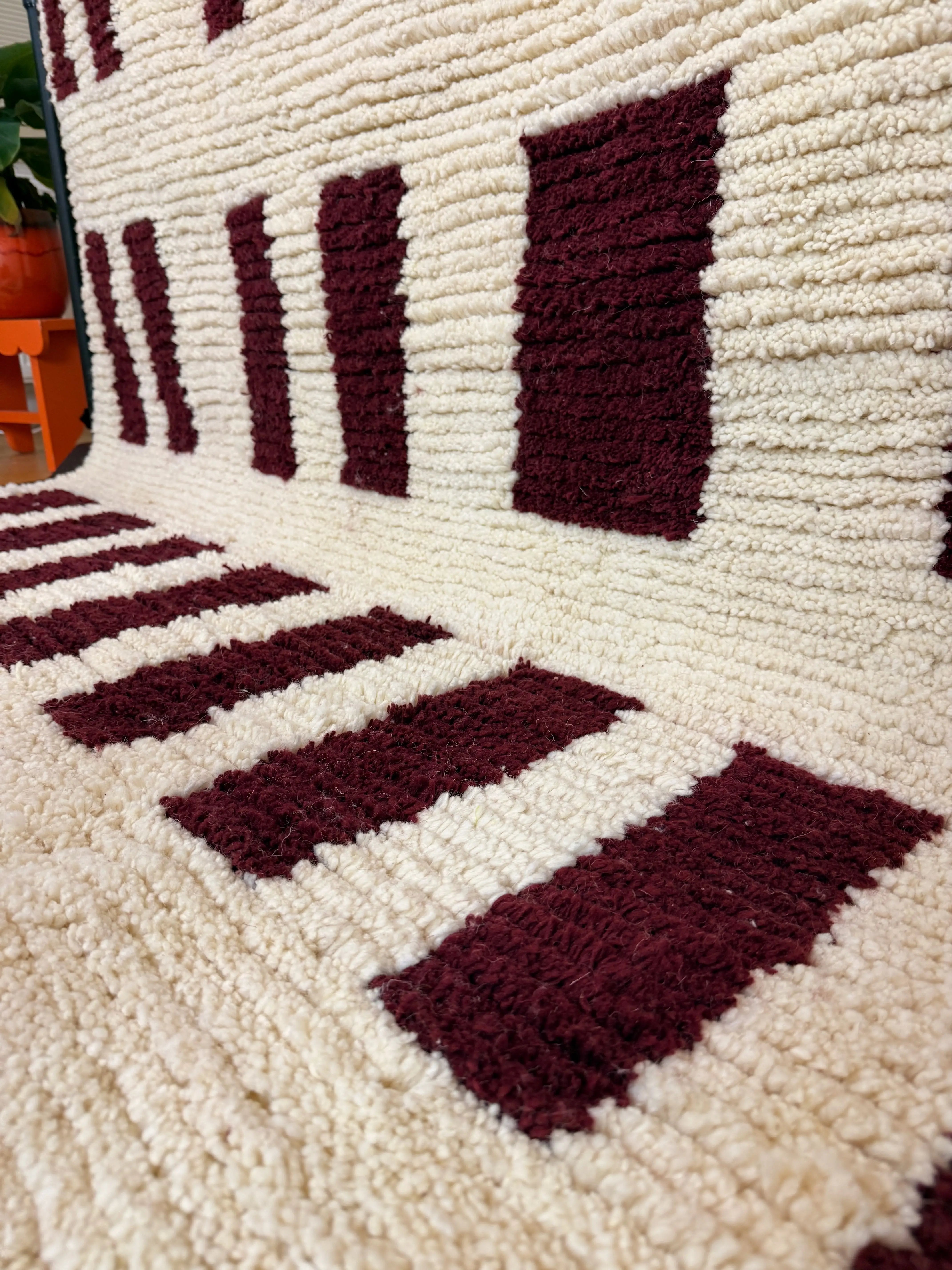 Close-up of the deep burgundy rectangle pattern and natural ivory wool pile on the Narjess handmade Berber rug, showing hand-knotted texture, Tunisia.