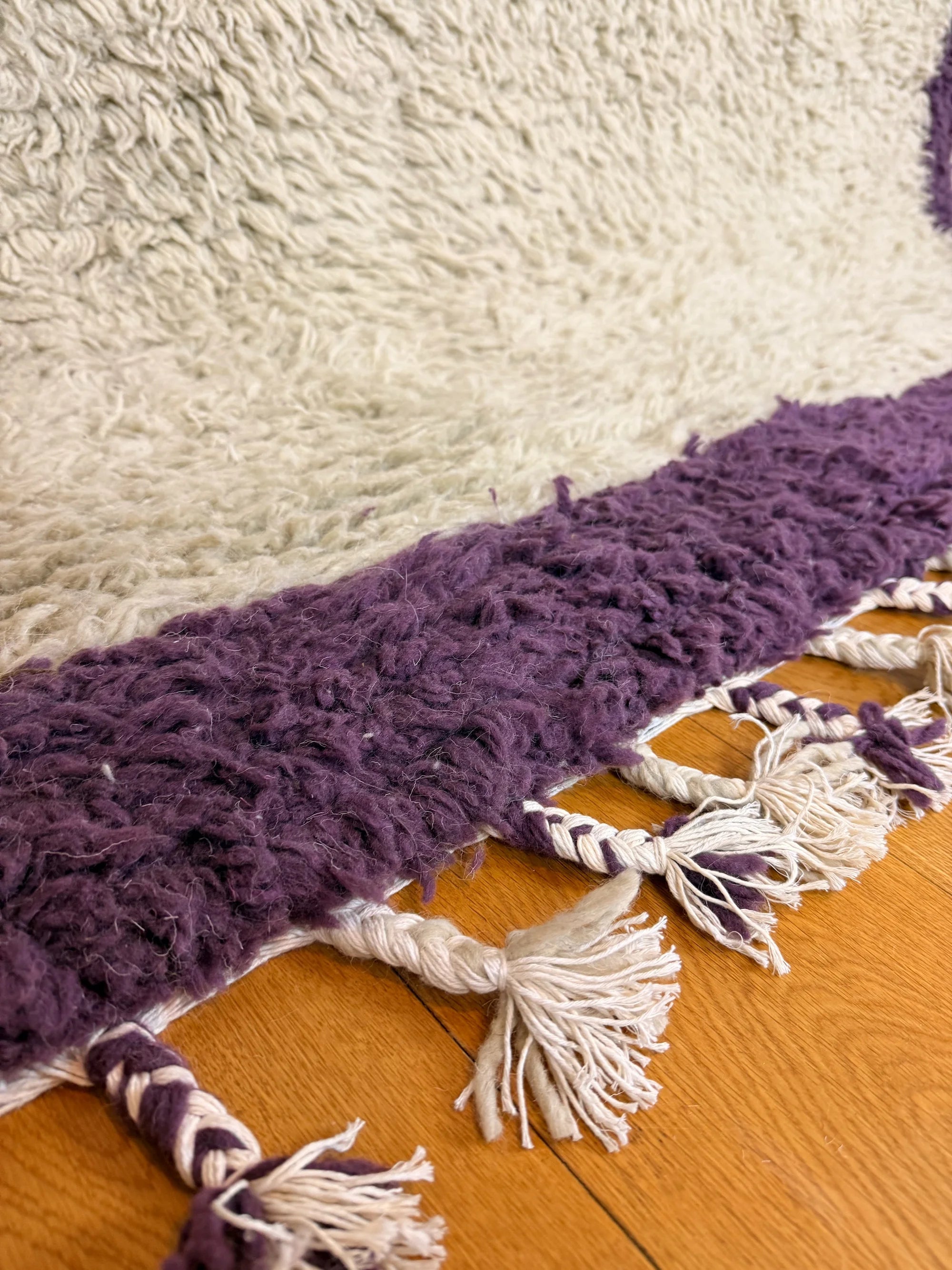 Close-up of the hand-knotted fringe tassels and deep purple border on the Zohra handmade shaggy Berber wool rug, Tunisia.