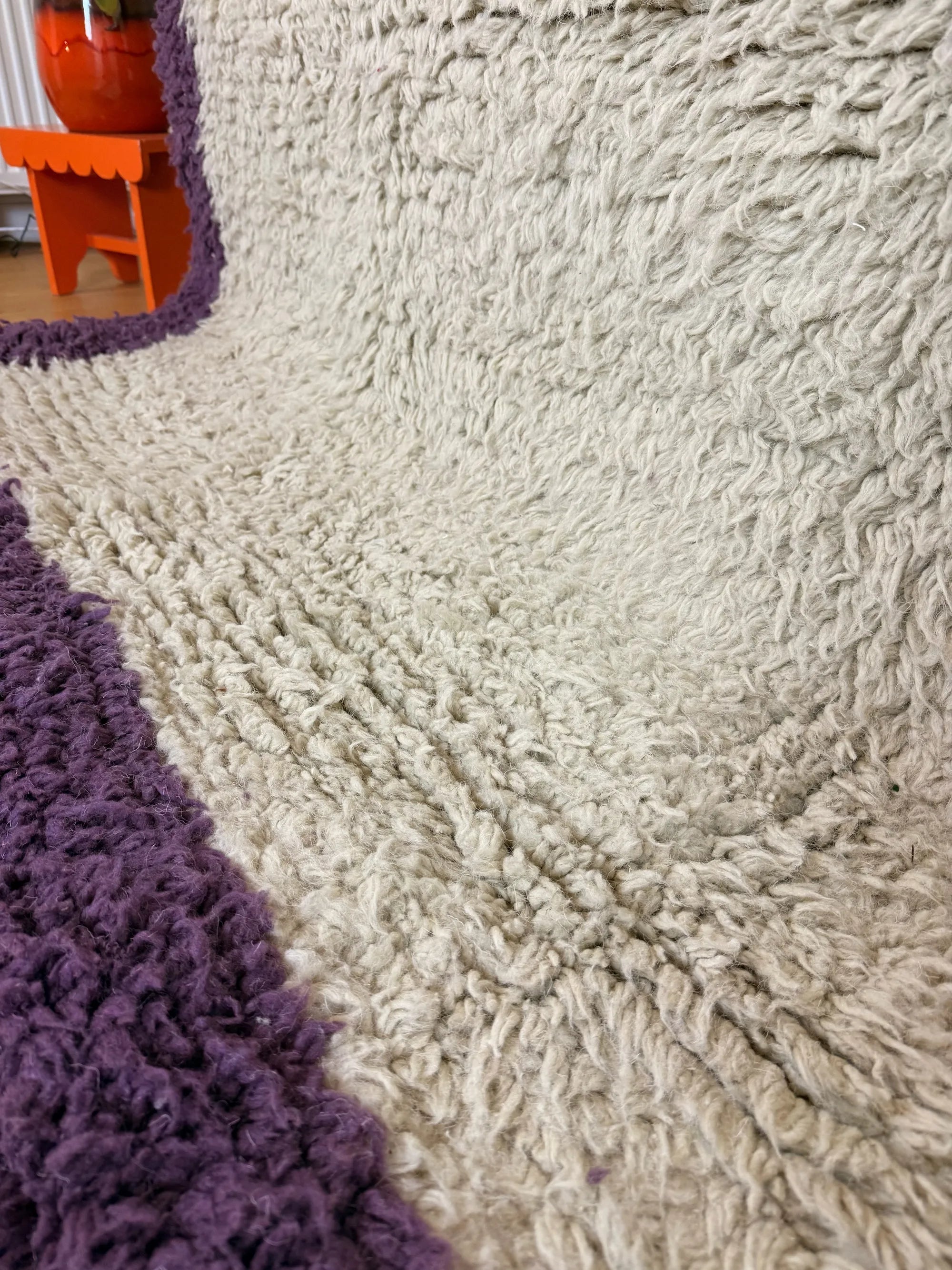 Macro close-up of the natural cream shaggy wool pile on the Zohra Berber rug, showing the dense hand-knotted texture next to the purple border, handmade in Tunisia.