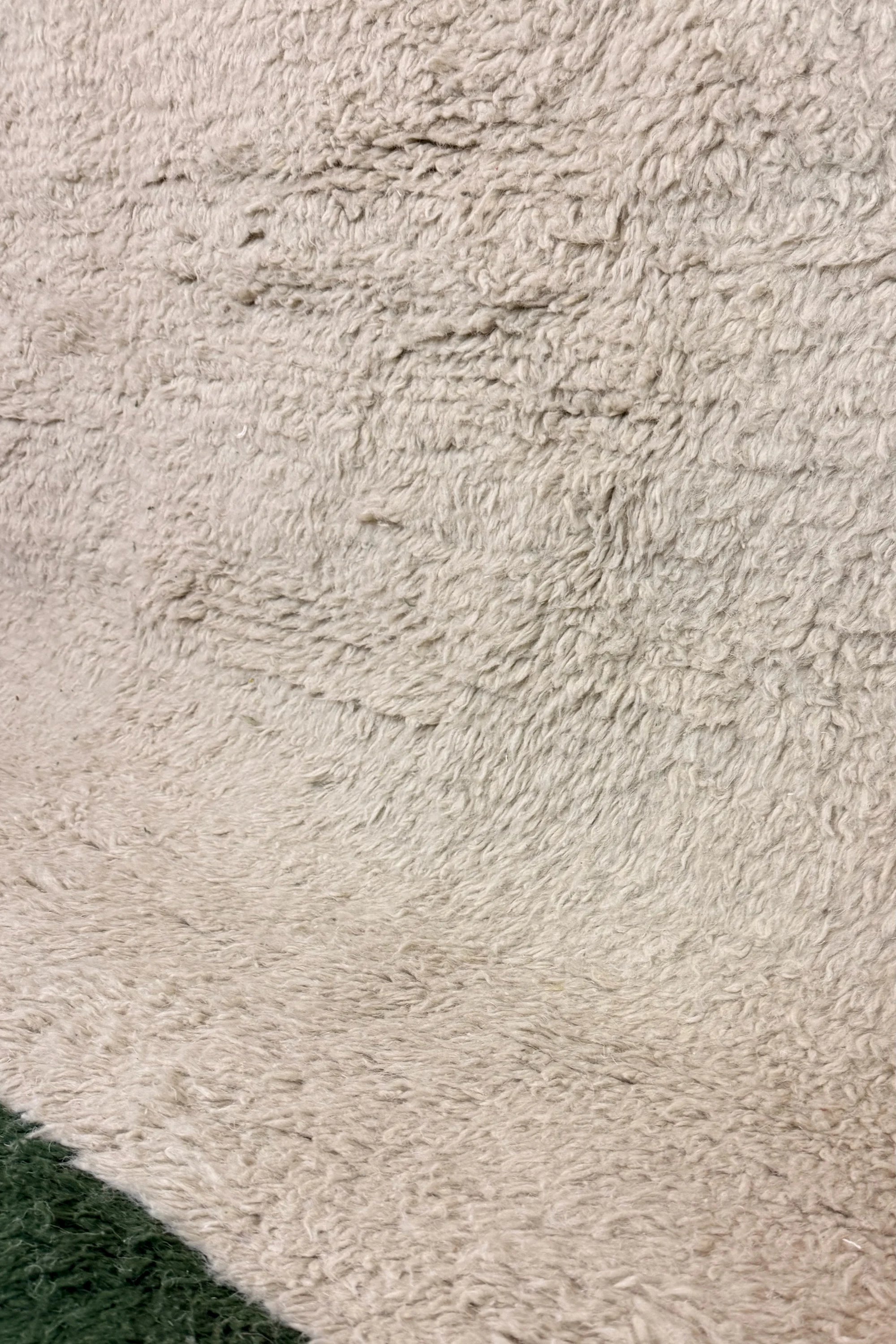 Close-up of the Bochra handmade Berber rug showing the transition between the natural cream wool centre and the forest green border, Tunisia.