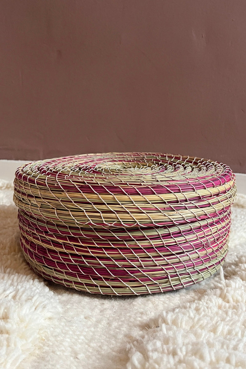 Woven basket with pink and green pattern on a textured surface