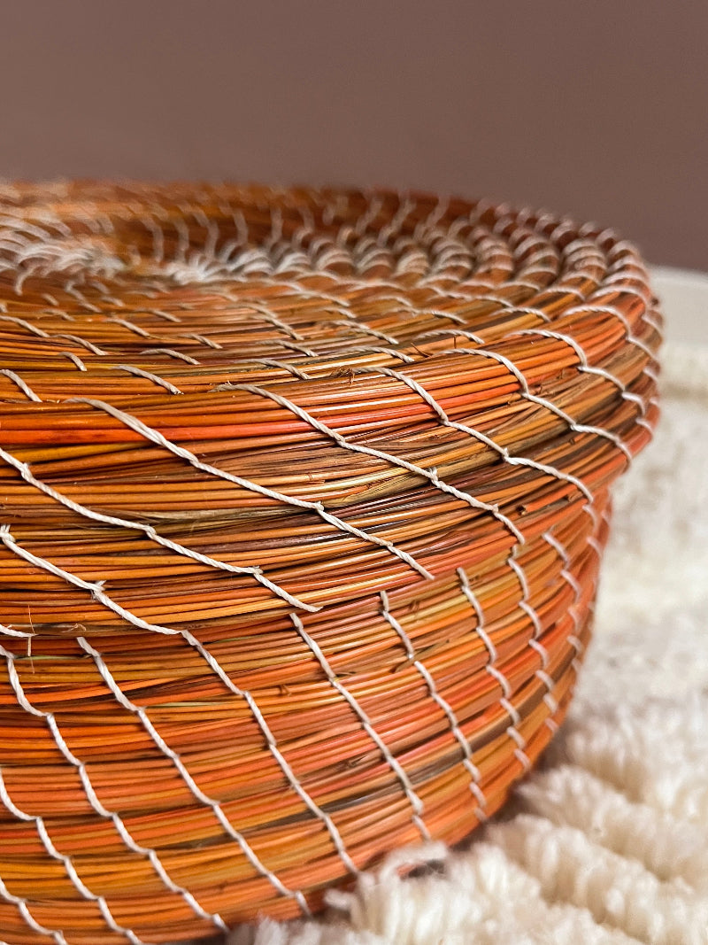 Angled detailed view of orange handwoven straw basket.