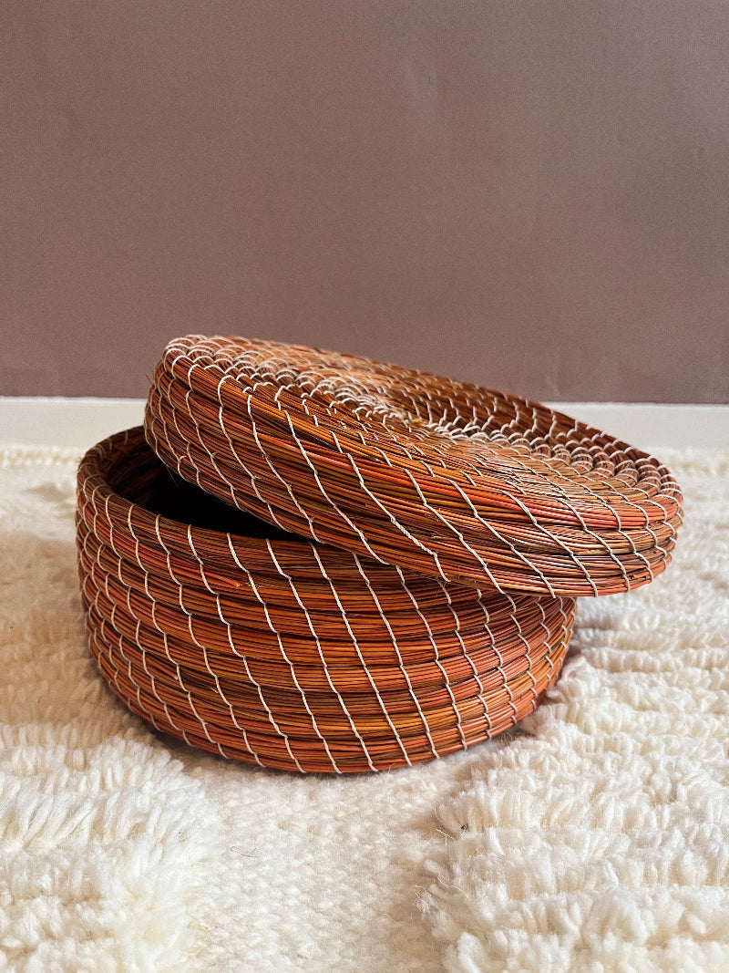 Orange straw basket with lid tilted open, showing interior and weave detail.