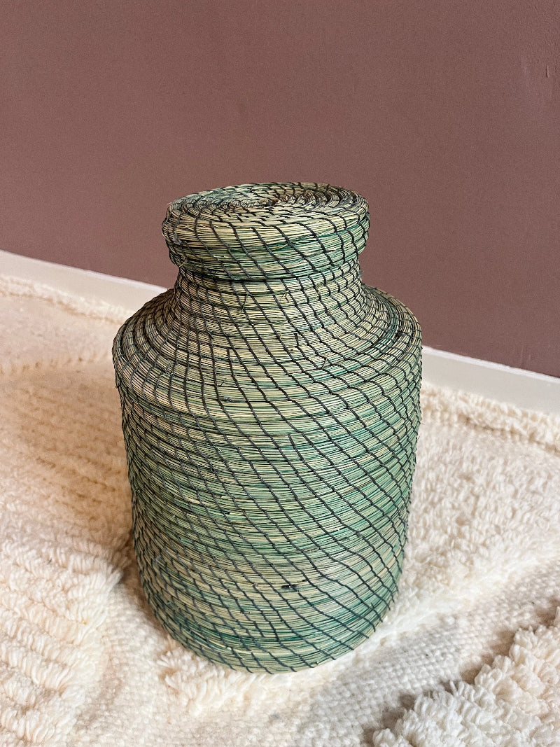 Angled view of green handmade straw basket Nabila with lid.