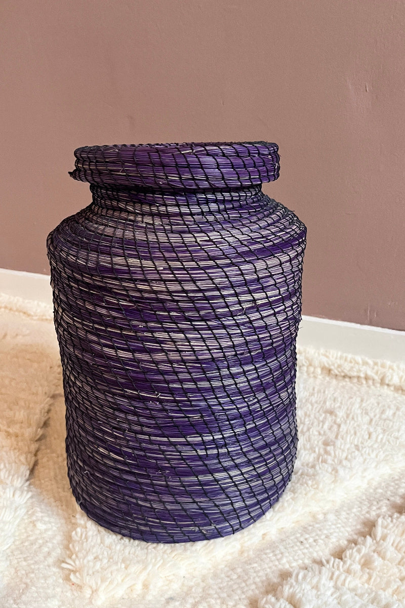 Handmade straw basket Nabila in deep purple with lid, full view on a textured surface with a plain background