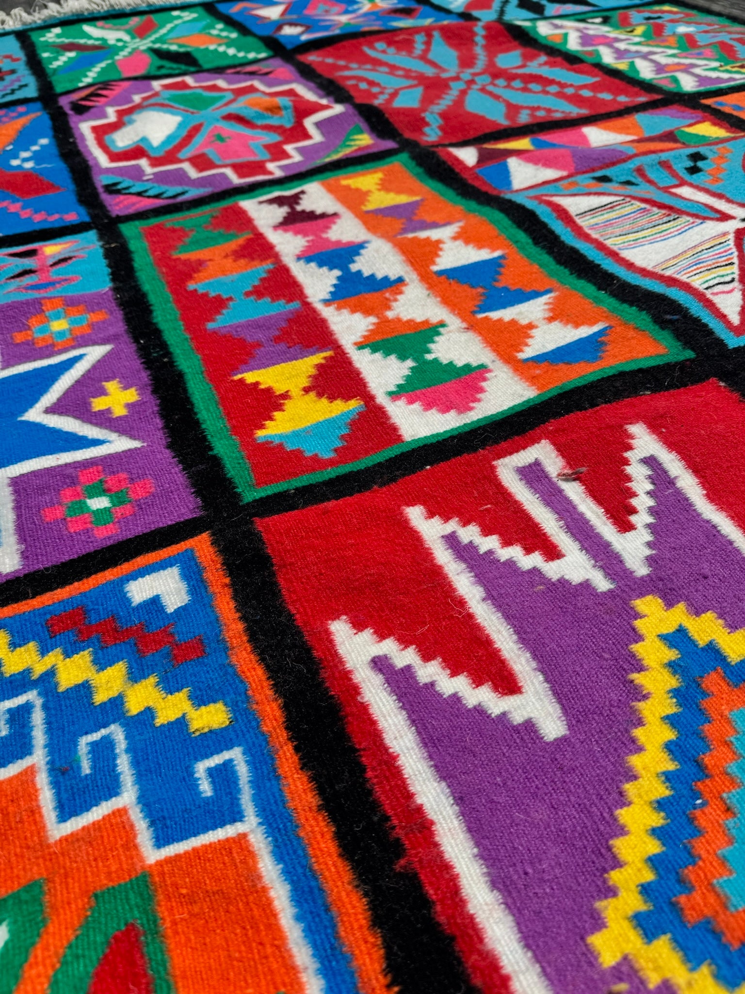 Angled close-up of wool rug showing multicolor patchwork design.