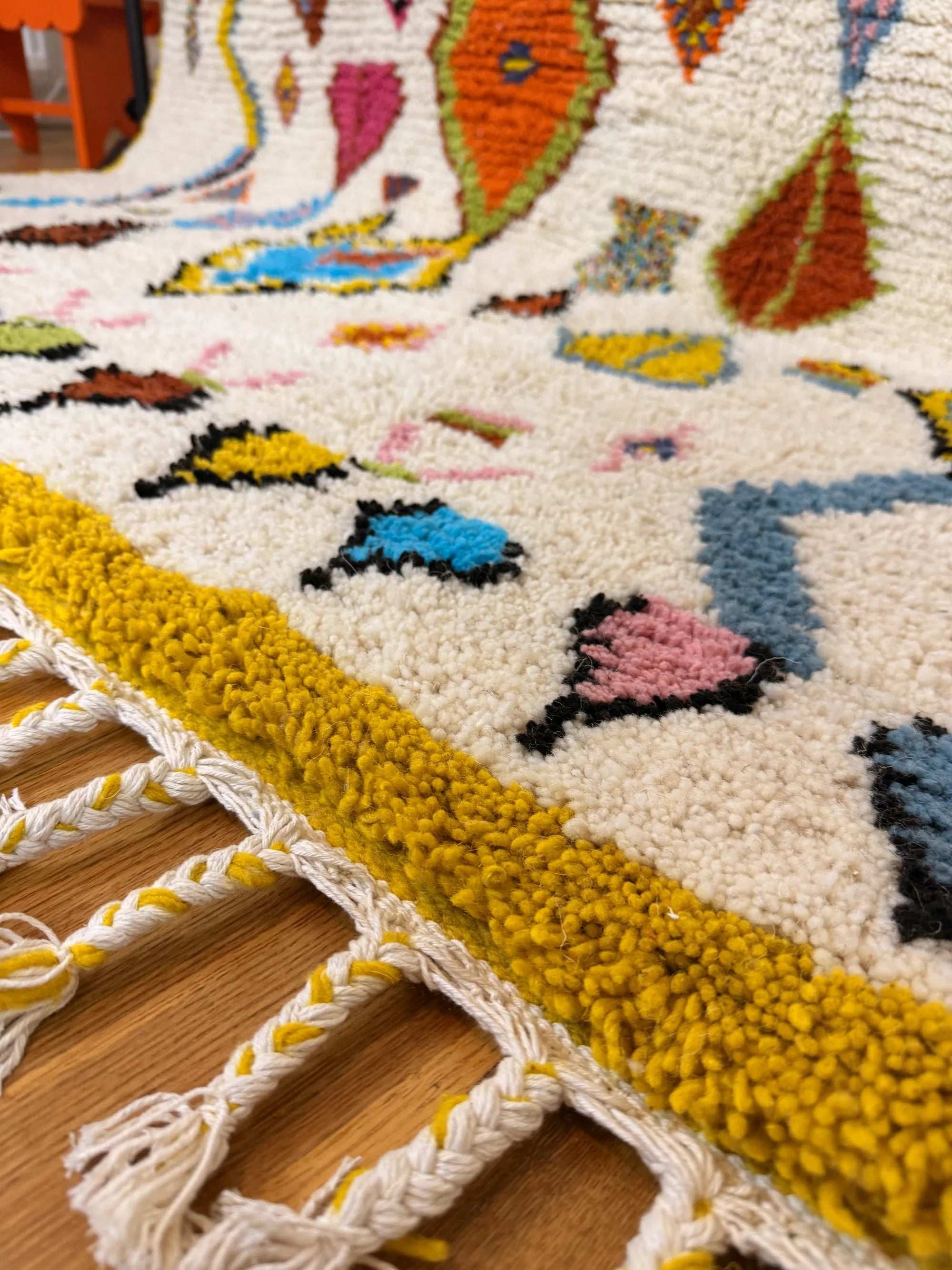 Close-up of the Khadija Berber wool rug showing the mustard yellow border, multicolour Amazigh motifs and hand-knotted fringe, handmade in Tunisia.