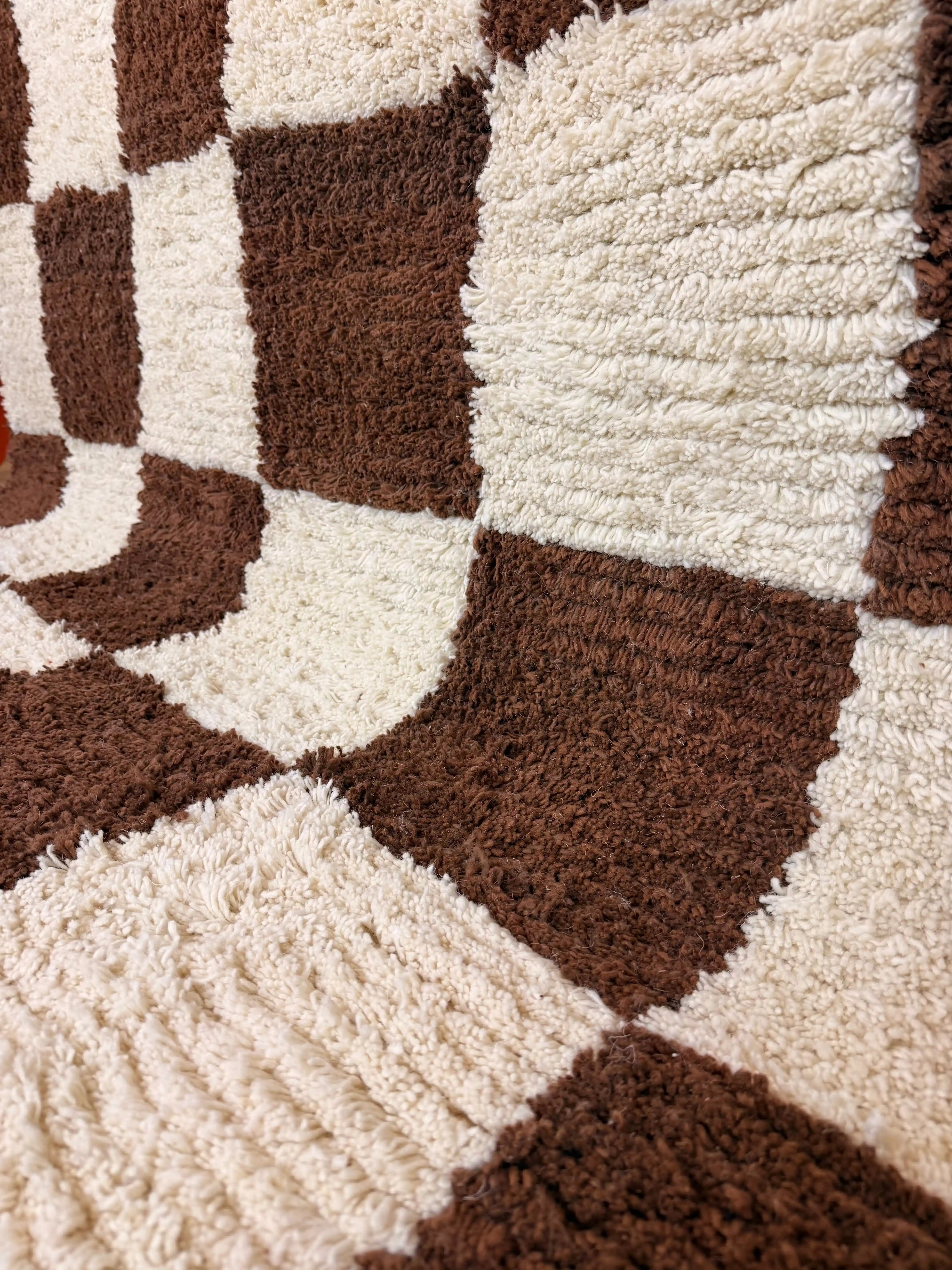 Angled close-up of Meriem handmade Berber wool rug, showing the rich texture and depth of the brown and cream checkerboard weave, Tunisia.