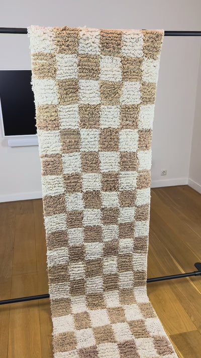 Sabrine handmade Berber wool runner from Tunisia, showing the camel beige and cream checkerboard pattern and looped pile texture in motion, 240 × 70 cm.
