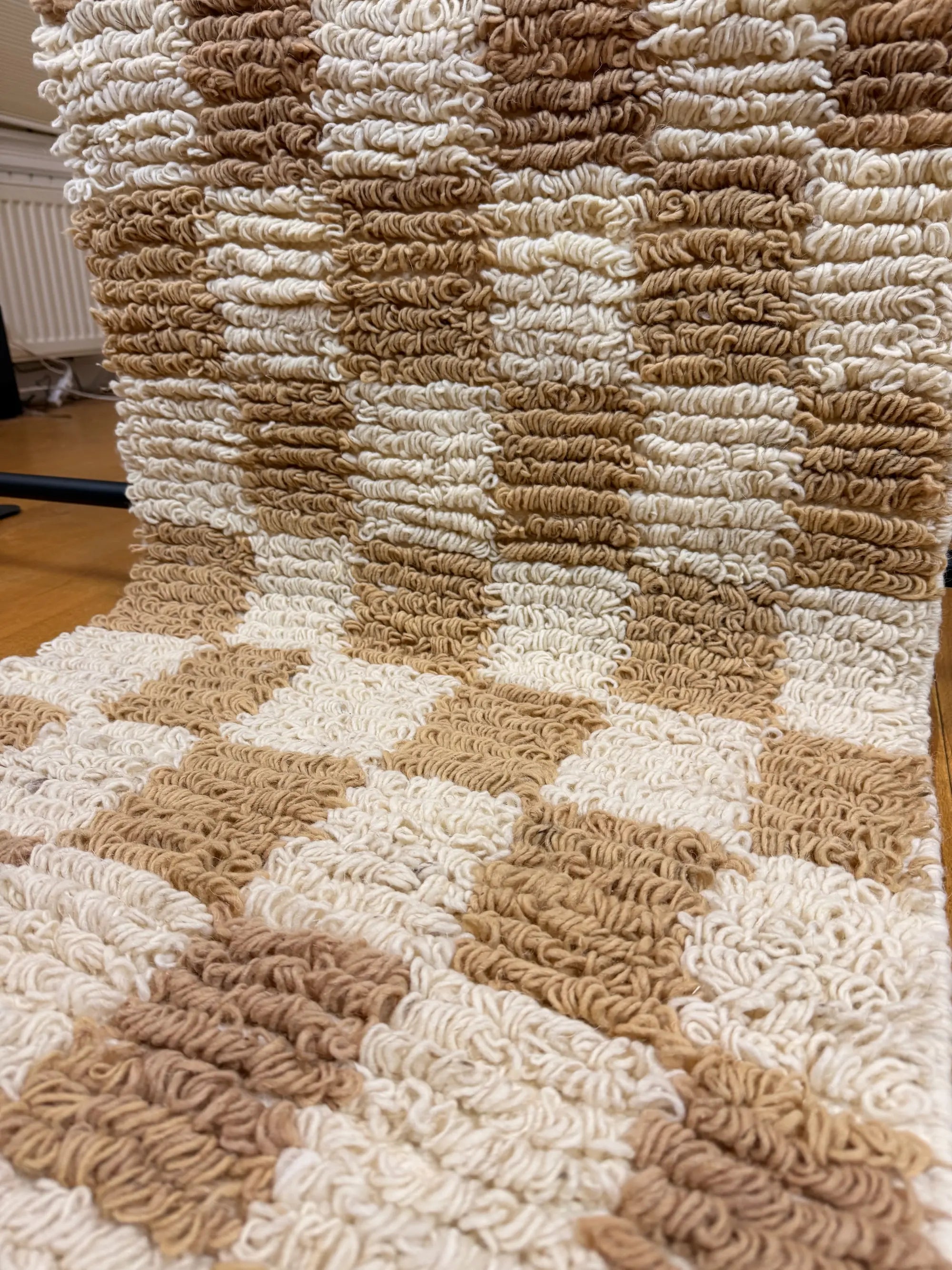 Close-up of the chunky looped wool pile on the Sabrine Berber runner, showing the sculptural camel beige and cream checkerboard texture, handmade in Tunisia.