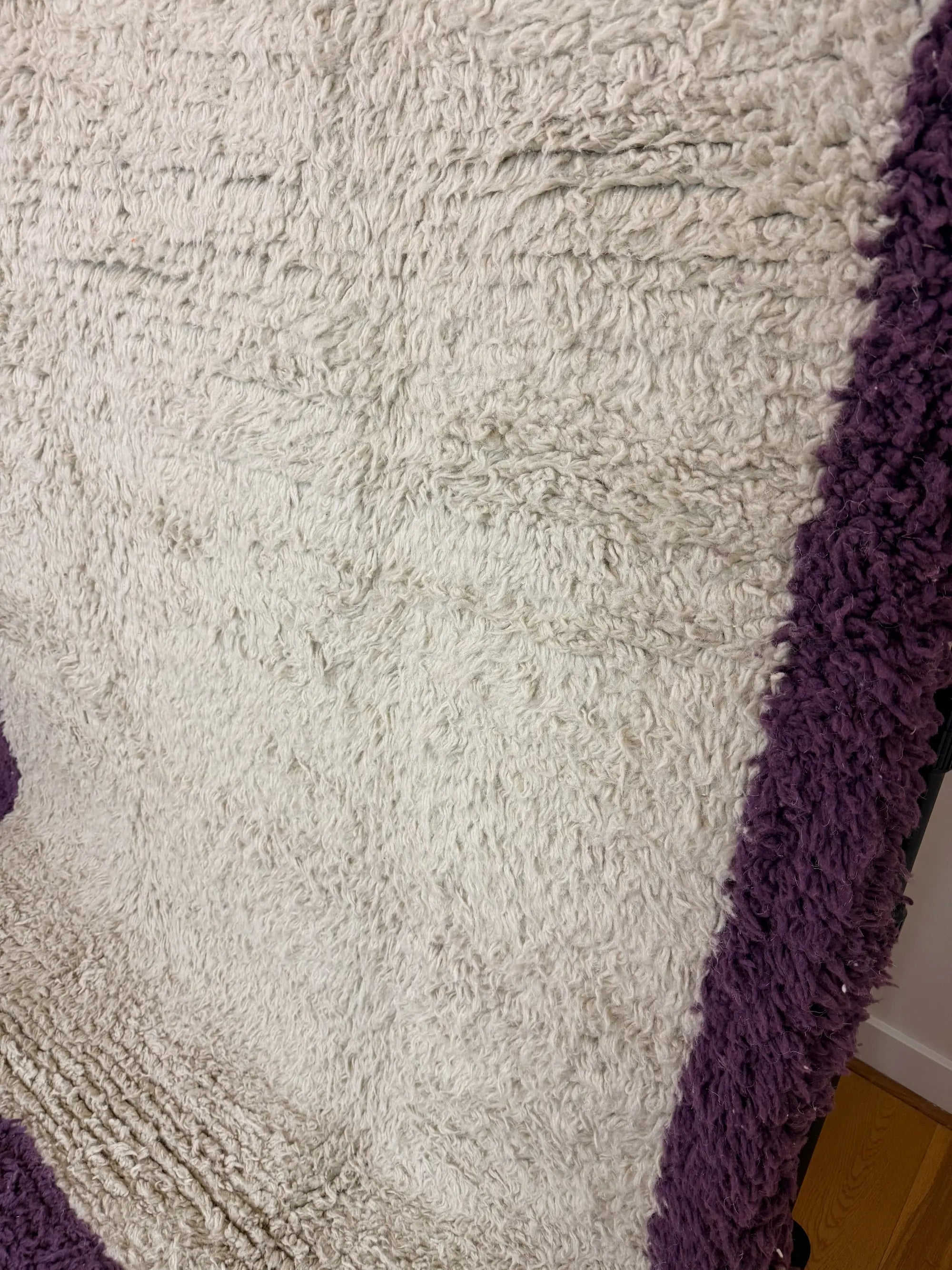 Angled close-up of the Zohra Berber wool rug showing the natural cream pile and deep purple border edge, handmade in Tunisia.
