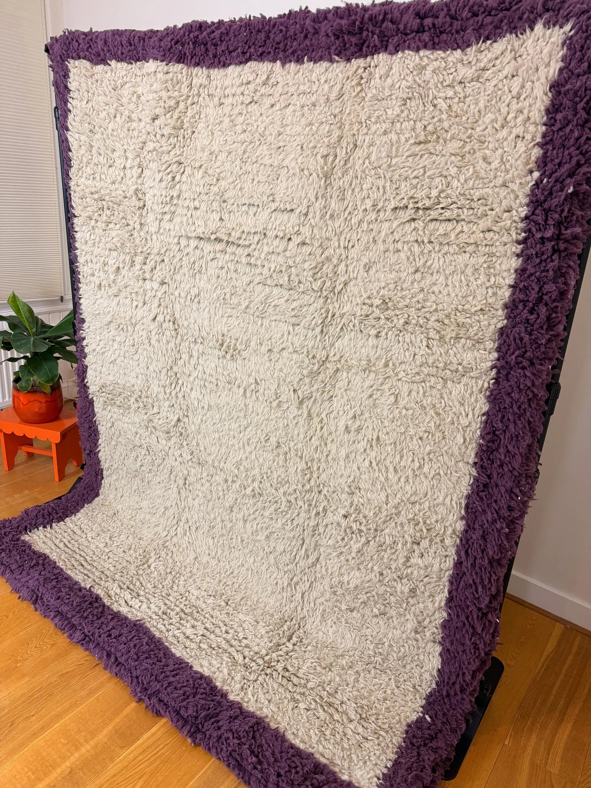 Zohra handmade shaggy Berber wool rug, side view showing the full cream centre framed by a deep purple border, handmade in Tunisia.